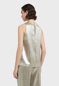 Metalni srebrni bezrukavni top s visokim izrezom, detaljem u obliku ključanice na leđima i glatkom teksturom, uparen s odgovarajućim hlačama.