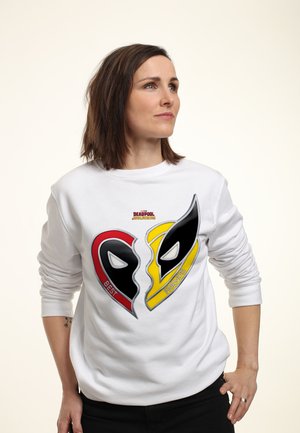 Femme portant un sweat-shirt blanc avec un motif de cœur brisé présentant les masques de Deadpool et Wolverine et le texte Meilleurs amis.