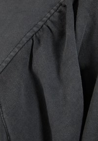 Tejido gris que muestra una superficie texturada con sutiles pliegues a lo largo de la costura, lo que indica un material suave y ligero.