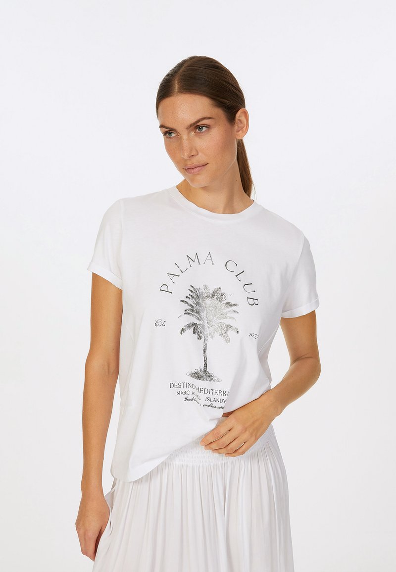 Weißes Baumwoll-T-Shirt mit einem metallischen Palmbaum-Graphic und dem Text "PALMA CLUB". Kurze Ärmel und lockere Passform. Kombiniert mit einem hellen Rock.