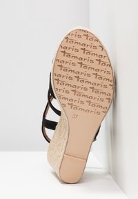 Sandale compensée avec des brides noires, une plateforme tissée beige et une semelle embossée à plusieurs reprises avec "Tamaris" et la taille 37.
