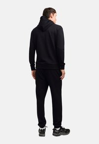 Black hoodie and sweatpants set made of soft fabric. Features a hood, ribbed cuffs, and relaxed fit. Shoes are dark with white accents.