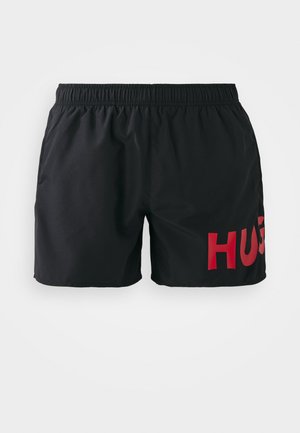 Sorte svøm shorts med elastisk talje og stort rødt "HUG" grafik på venstre side. Materialet ser let og glat ud.