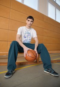 Camiseta blanca con un gráfico de baloncesto y el texto "SÓLO HAZLO", combinada con pantalones sueltos azul claro y zapatillas negras y azul claro, sosteniendo un balón de baloncesto.