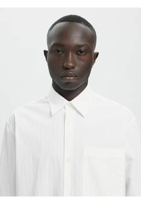 Weiß gestreiftes Hemd mit klassischem Kragen, durchgehender Knopfleiste und einer einzelnen Tasche auf der linken Brustseite. Der Stoff wirkt leicht und strukturiert.