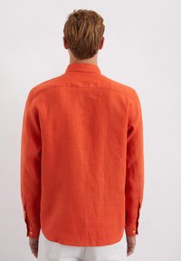 Orange linen button-up shirt with a traditional collar, elongated back hem, and long sleeves featuring buttoned cuffs.