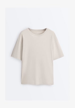 Prosty beżowy bawełniany T-shirt z krótkim rękawem, okrągłym dekoltem i luźnym krojem, prezentowany na białym tle.