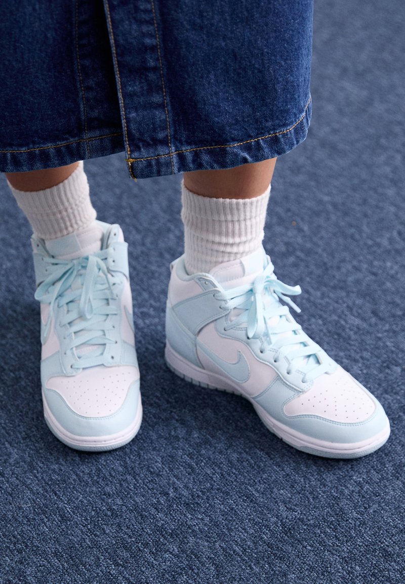Sneakers alte in azzurro chiaro e bianco con punta perforata e lacci abbinati, indossati con calze bianche a coste e una gonna di jeans.