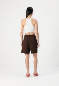 Brune tilpassede shorts med høy midje, som viser sidelommer. Modellen har på seg en hvit kort top og røde hælsandaler.