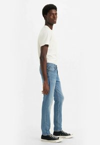 Vit t-shirt med kort ärm, ljusblå jeans och svarta sneakers. Jeansen har en klassisk passform och subtila sömdetaljer.