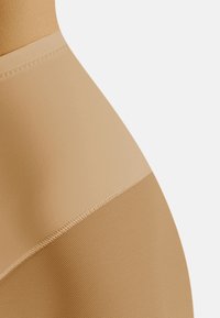 Beige színű, varrás nélküli bodysuit, sima felső résszel és texturált alsó résszel, varrással kiemelt átmenettel.