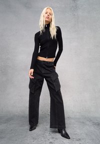 Top corto de canalé negro con cremallera, combinado con pantalones cargo negros con grandes bolsillos, complementado con botas de tobillo negras con punta.