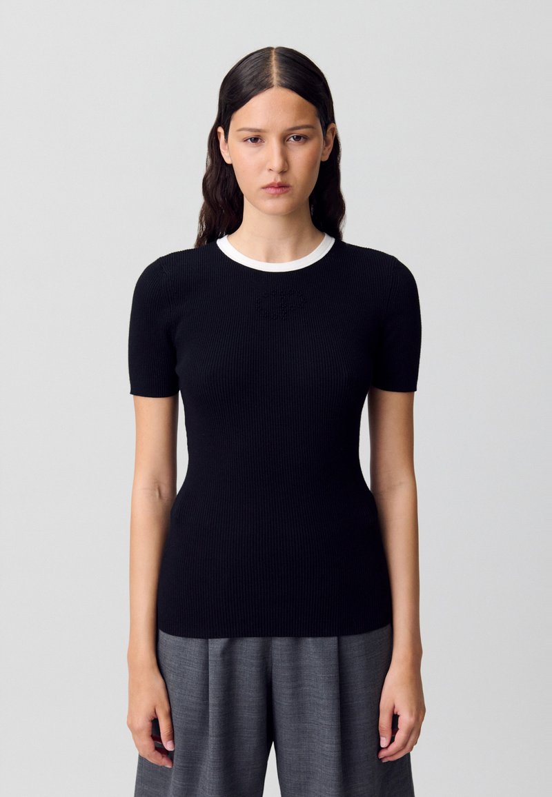 Top corto de punto acanalado negro con cuello redondo blanco y un sutil detalle de texto. Combinado con pantalones de talle alto grises.
