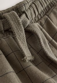 Close-up of olive green knit pants with a checkered pattern, featuring a textured drawstring and elastic waistband.
