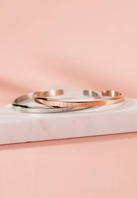 Deux bracelets en métal, l'un argenté et l'autre en or rose, arborant le texte gravé "VICTORIA HYDE", présentés sur une surface en marbre clair.
