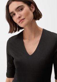 Zwarte aansluitende top met een diepe V-hals en korte mouwen, gemaakt van een soepel materiaal, met een schone, minimalistische uitstraling.