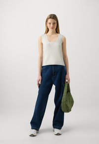 Valge kudumista tank top avatud kaelusega, millele on lisatud laiad sinised teksapüksid. Käes on roheline vatitud käekott.