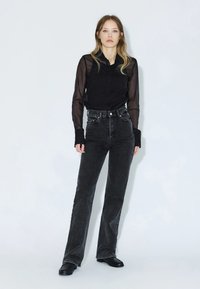 Camicia nera trasparente a maniche lunghe con colletto, abbinata a jeans neri a vita alta e stivali neri. Silhouette piatta con maniche aderenti.