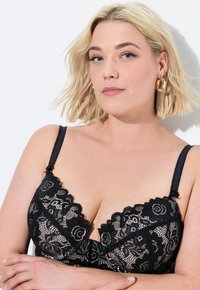 Zwarte kanten beha met bloemmotieven, gegolfde randen en verstelbare bandjes. Het materiaal heeft een delicate textuur en verfijnde details.