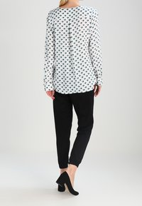 Long-sleeve white blouse with teal leaf print, paired with black tapered pants and black suede heels. Smooth fabric, relaxed fit.