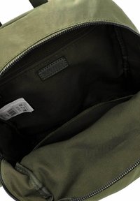 Interior de mochila verde oliva, hecho de tela con una textura suave. Presenta un cierre con cremallera y una pequeña etiqueta de marca en el interior.