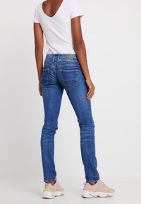 Smal blå denimjeans med hög midja, med två bakfickor. Ihopkopplad med en vit ribbad topp och ljusa träningsskor.