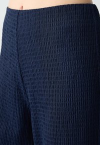 Pantalons bleu marine texturés avec une surface froissée. Le tissu est léger, créant une silhouette décontractée avec une taille élastique.