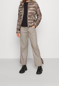 Pohodlná hnědá bunda s umělou kožešinou na kapuci, kombinovaná s širokými kalhotami s kostkovaným vzorem. Černé chunky boty dotvářejí celý vzhled. Přítomný kontrast textury a barev.