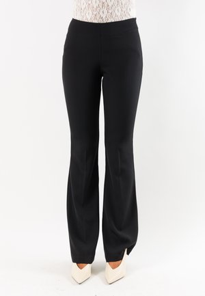 Donna che indossa pantaloni neri aderenti a zampa abbinati a décolleté bianchi con punta e un top bianco in pizzo visibile in vita.