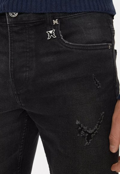 Jeans in denim nero con una texture strappata e una lacerazione visibile, accentuati da un bottone con logo argento e un delicato ricamo.