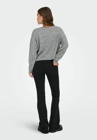 Pull en tricot gris à coupe décontractée et décolleté bateau, associé à un jean noir évasé avec une taille mi-haute et des poches arrière.