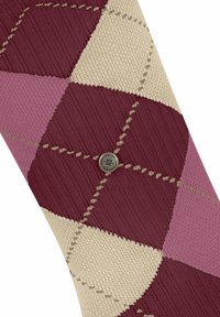 Gestrickte Socke mit einem Argyle-Muster in Burgunderrot, Pink und Beige. Sie hat eine strukturierte Oberfläche und ein metallisches Markenakzent.