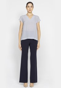 Niebiesko-biała bluzka z krótkim rękawem w wzory, z dekoltem w kształcie litery V, w połączeniu z granatowymi spodniami szerokimi i beżowymi szpilkami. Gładka tekstura materiału.
