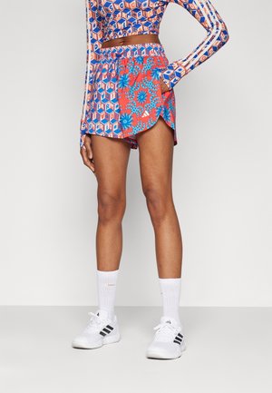 Bright patterned sportswear set featuring a long-sleeve top with geometric designs and shorts with floral accents, in blue and red tones.