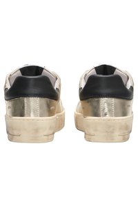 Sneakers dorati e neri con una finitura metallica testurizzata, suole in gomma e colletto imbottito. Dettagli usurati vicino alla suola.