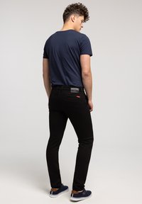 Czarne obcisłe dżinsy z skórzaną naszywką na tylnej części pasa, zestawione z dopasowaną granatową koszulką i ciemnoniebieskimi butami.