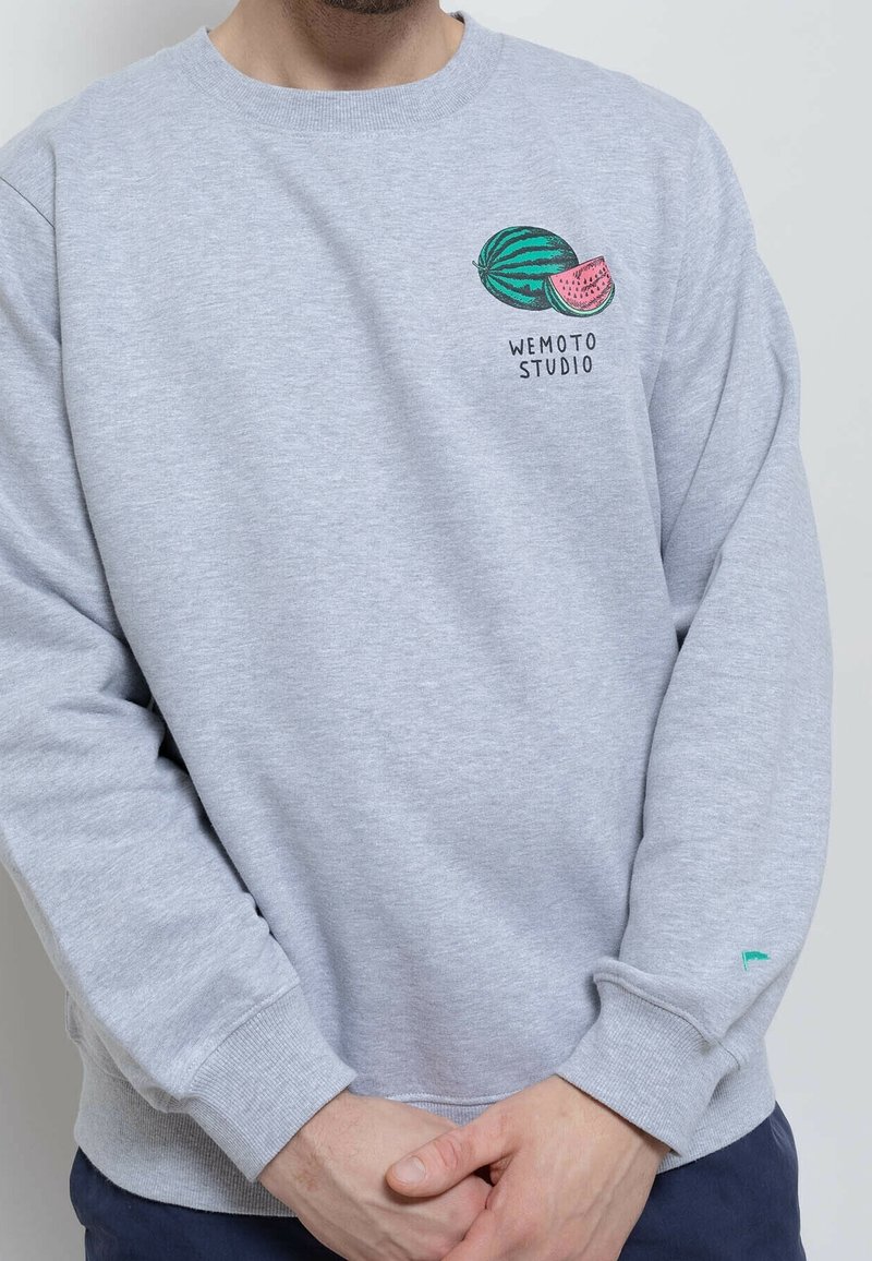 Sweat-shirt gris avec un motif de pastèque brodé et le texte "WEMOTO STUDIO". Poignets et ourlet côtelés, avec un petit accent vert sur la manche.