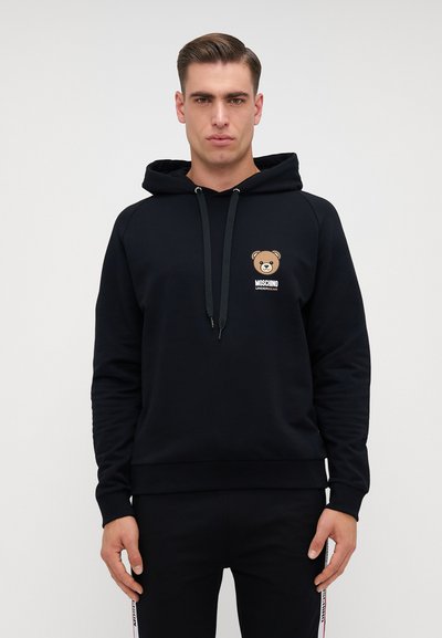 Hoodie noir en matériau doux avec un graphique d'ours sur le devant et une capuche à cordon. Présente des poignets et un ourlet côtelés pour un look ajusté.