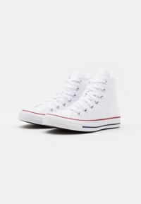 Białe kanvasowe sneakersy za kostkę z srebrnymi oczkami, czerwono-niebieską gumową podeszwą w paski, okrągłym noskiem i teksturowanym materiałem.