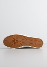 Semelle d'une chaussure en caoutchouc marron avec un motif décoratif et le nom de la marque "JOOP!" embossé près du talon.