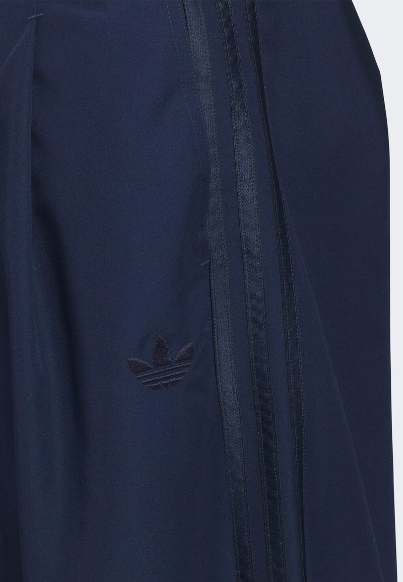 Tela azul marino con un sutil logo Adidas Trefoil y tres franjas de satén negro que corren verticalmente a lo largo del costado.