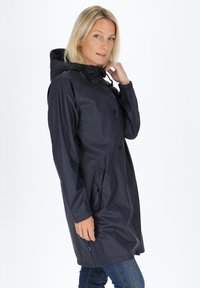 Granatowy wodoodporny płaszcz przeciwdeszczowy z kapturem, z przodu zapinany na guziki, z elastycznymi mankietami i bocznymi kieszeniami, charakteryzujący się gładką teksturą i średniej długości krojem.