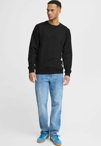 Zwarte sweatshirt met een ronde hals en geribbelde manchetten, gecombineerd met lichtblauwe denim jeans en blauwe sneakers. Eenvoudig ontwerp, geen patronen.