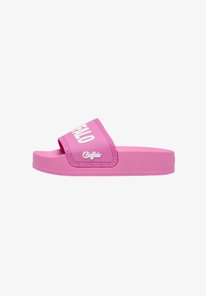 Persona che indossa pantaloni verde oliva e ciabatte platform rosa acceso con scritta bianca "BUFFALO", in piedi su un marciapiede urbano soleggiato.