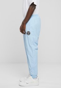 Light blue, lightweight athletic pants with side pockets and elastic waistband, featuring a black circular logo on the left leg.