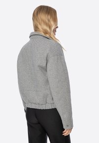 Graue Jacke mit Hahnentrittmuster, Kragen, kurzem Schnitt, elastischem Saum und Knopfdetail an den Ärmeln. Glatte Textur.