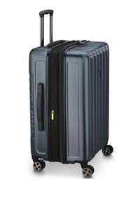 Valigia rigida di colore grigio scuro con scanalature verticali, manico telescopico, doppi zip e quattro ruote girevoli per una maggiore mobilità.