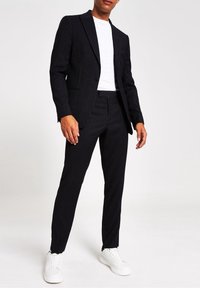 Svart kavajdräkt med en figursydd kavaj och byxor, i kombination med en vit t-shirt och vita sneakers. Slät tyg, skräddarsydd design.