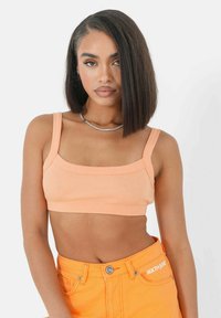 Perzik ribbel crop top met brede banden, vierkante halslijn en aansluitend ontwerp. Gepaard met hoog-getailleerde oranje shorts met een zilveren knoop.