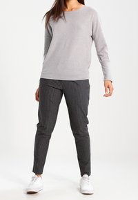 Szary sweter z długim rękawem i okrągłym dekoltem w połączeniu z czarnymi rurkowatymi spodniami w prążki. Całość dopełniają białe trampki.